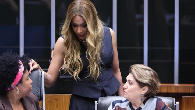 Deputada federal Érika Hilton em pé conversando com colegas no plenário da Câmara dos Deputados