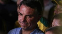 Flávio Bolsonaro em evento de campanha, com bandeira do Brasil ao fundo