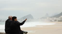 Duas pessoas agasalhadas, sentadas no calçadão, observam a praia de Copacabana num dia frio e nublado no Rio de Janeiro; imagem de arquivo, não é do dia do alerta