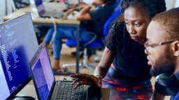 Duas pessoas olhando para tela de notebook com código de programação