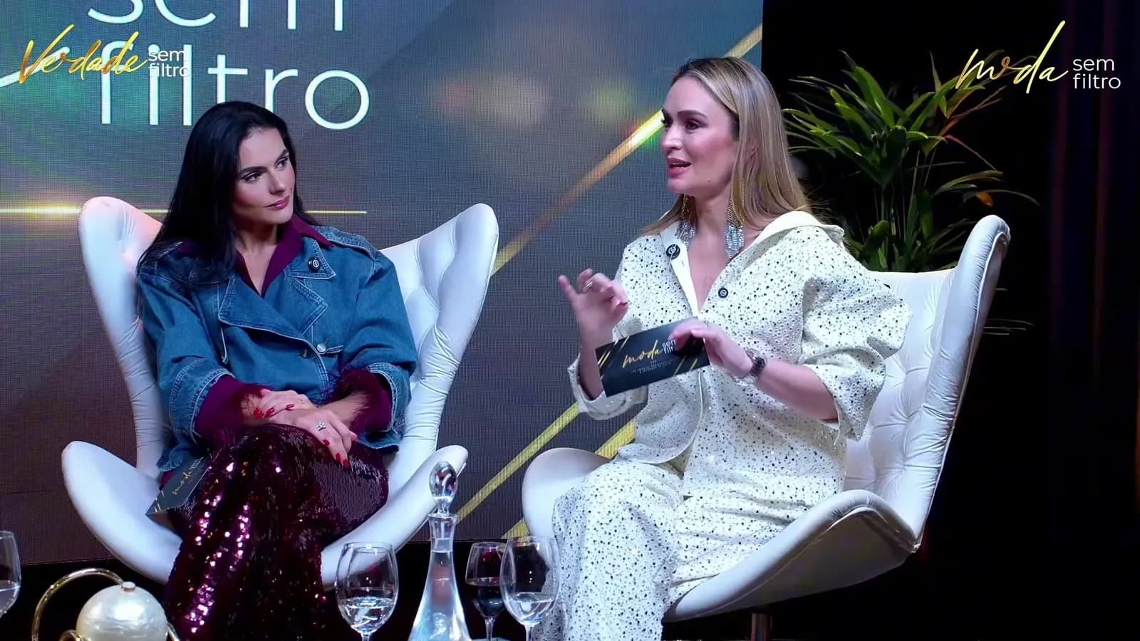 Duas apresentadoras do programa Moda Sem Filtro conversam sentadas em poltronas brancas do estúdio, durante o quadro Verdade Sem Filtro