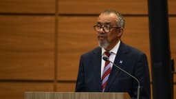 Tedros Adhanom, diretor-geral da OMS, de terno azul-marinho e gravata vermelha, fala ao microfone em um púlpito de madeira na Fiocruz, no Rio de Janeiro