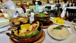 Mesa farta com pratos típicos mineiros servidos em panelas de barro, arroz e torresmo