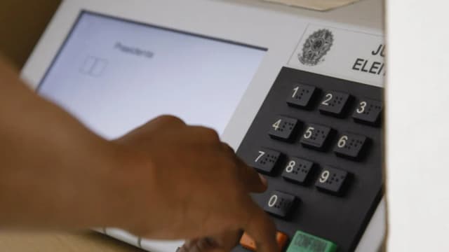 Mão de eleitor digita em urna eletrônica brasileira durante votação