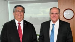 O ministro Flávio Dino sorrindo, de terno escuro e gravata vermelha
