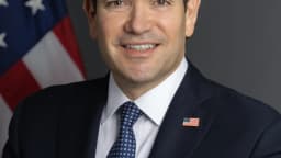 Retrato oficial do secretário de Estado dos EUA, Marco Rubio, sorrindo em frente a uma bandeira dos Estados Unidos