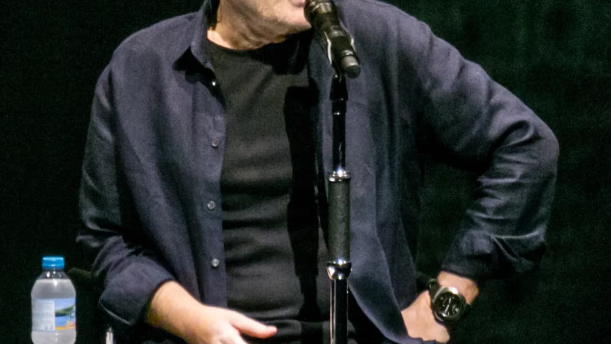 Phil Collins sentado ao microfone durante apresentação no Royal Albert Hall, em Londres