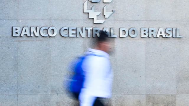 Letreiro metálico com a inscrição Banco Central do Brasil na fachada de granito da sede da autarquia, com um pedestre passando em primeiro plano. Imagem de arquivo