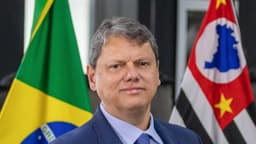Tarcísio de Freitas, de terno azul, ao lado das bandeiras do Brasil e de São Paulo