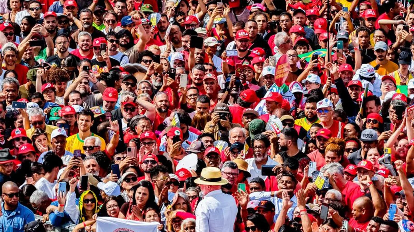 Lula, de chapéu e camisa branca, de costas diante de multidão com bandeiras e bonés vermelhos durante lançamento de campanha em São Bernardo do Campo
