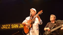 João Bosco canta e toca violão em show, usando boné branco