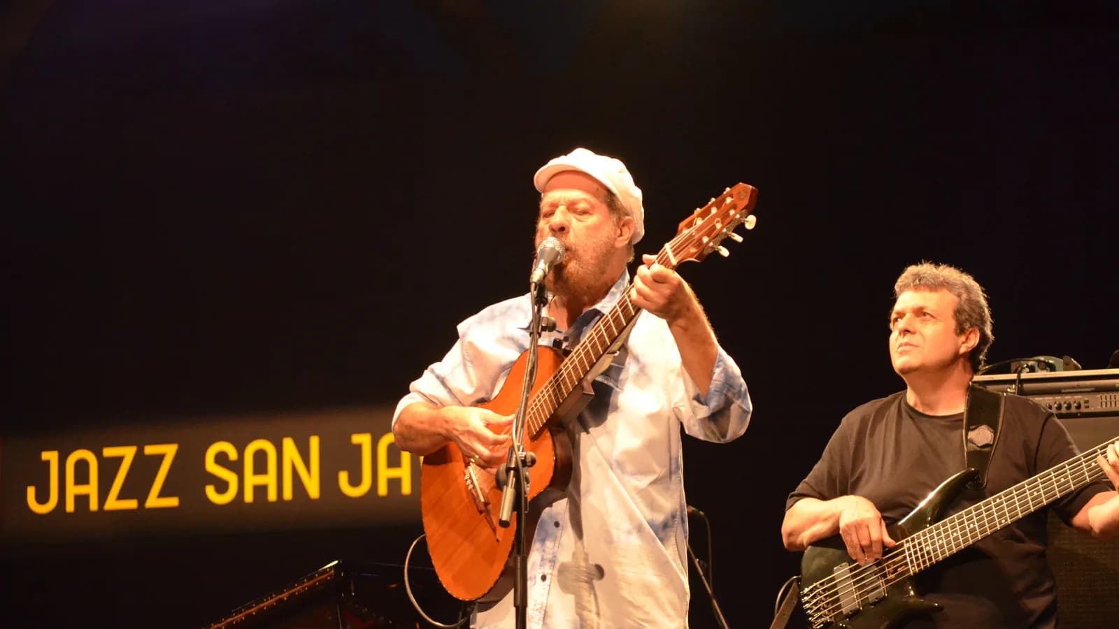 João Bosco canta e toca violão em show, usando boné branco