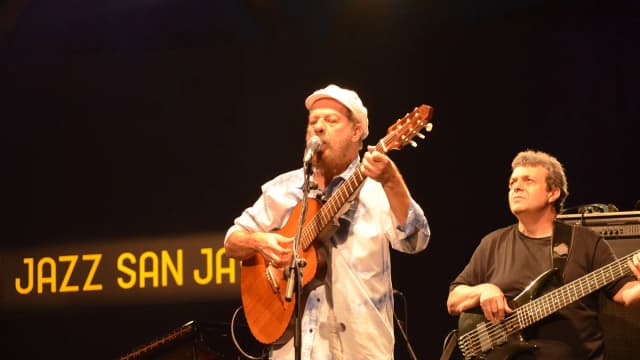 João Bosco canta e toca violão em show, usando boné branco