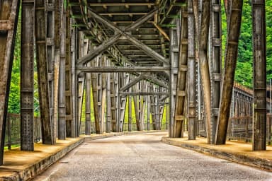 Imagem ilustrativa: Vista interna de um viaduto de metal com estrutura exposta e estrada pavimentada sob um céu claro e vegetação ao fundo
