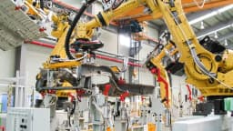 Braços robóticos amarelos em linha de montagem industrial