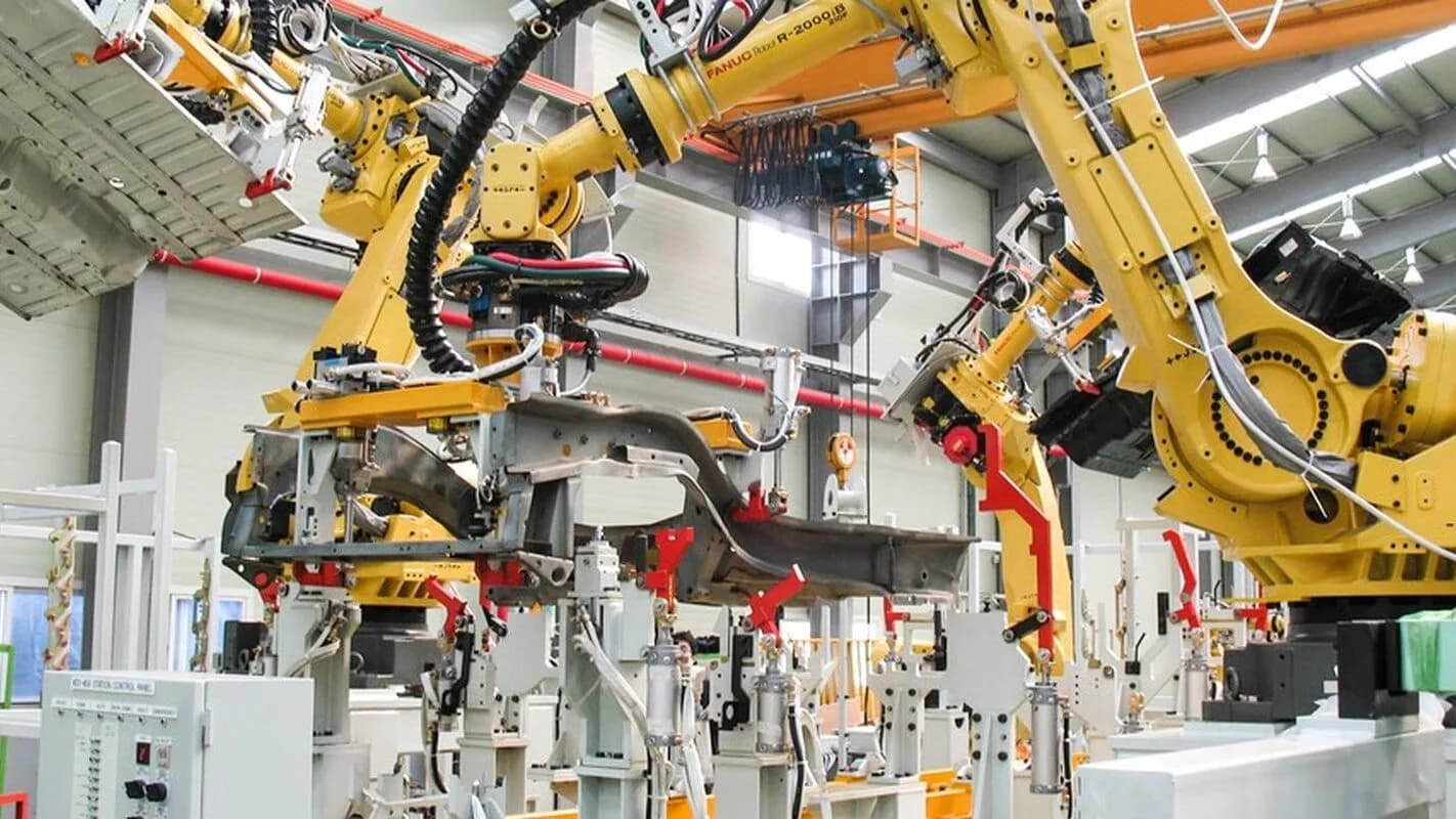 Braços robóticos amarelos em linha de montagem industrial