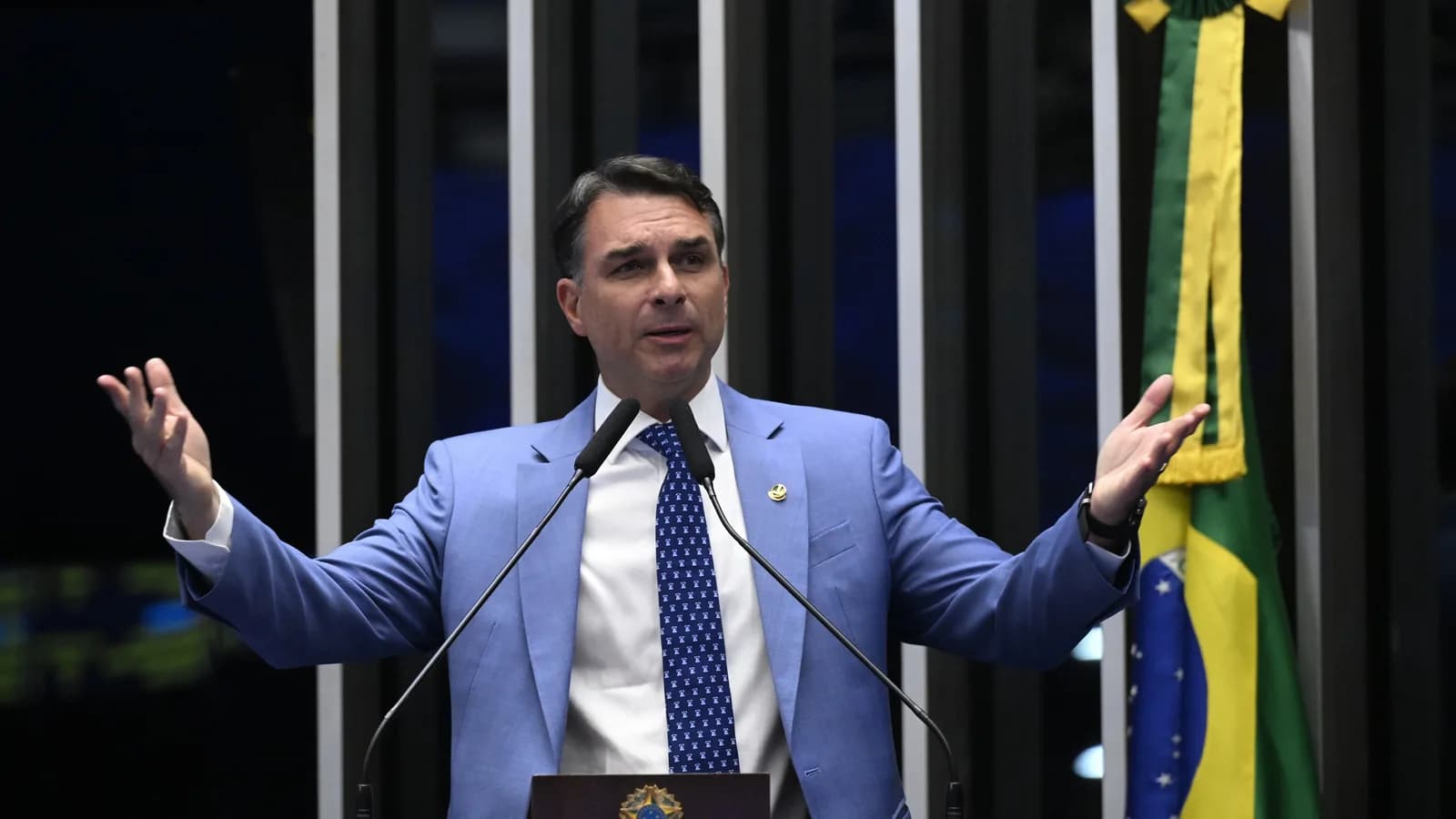 Senador Flávio Bolsonaro discursa no plenário do Senado com bandeira do Brasil ao fundo