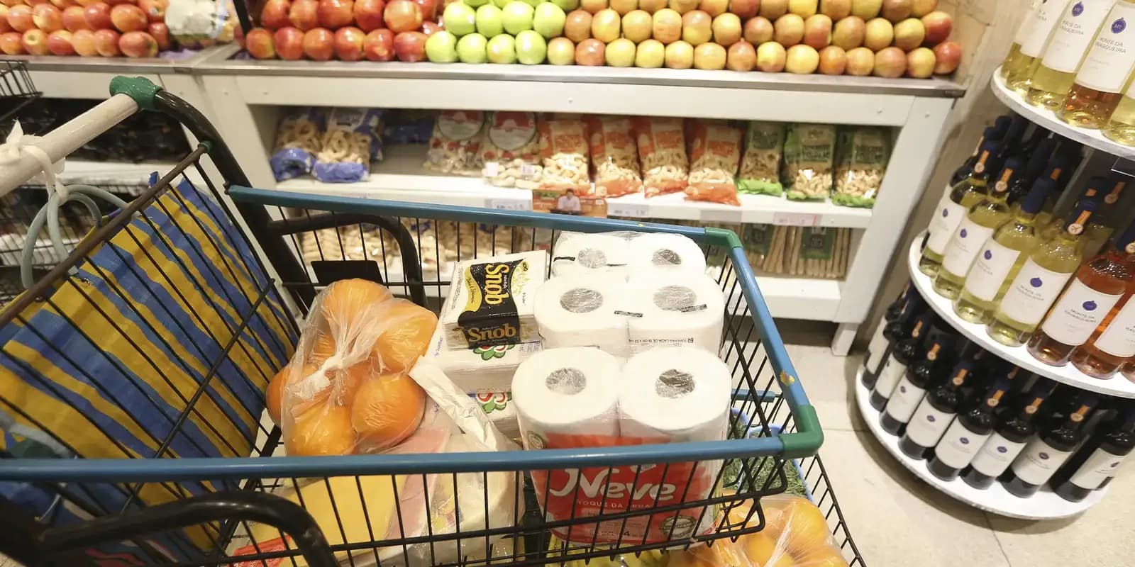 Carrinho de supermercado com alimentos e produtos de limpeza em corredor de loja