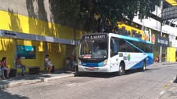 Ônibus da Saritur parado em ponto de transporte coletivo, com passageiras aguardando no banco ao lado