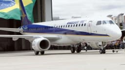 Jato da Embraer estacionado em pátio, com bandeira do Brasil ao fundo (foto de arquivo)