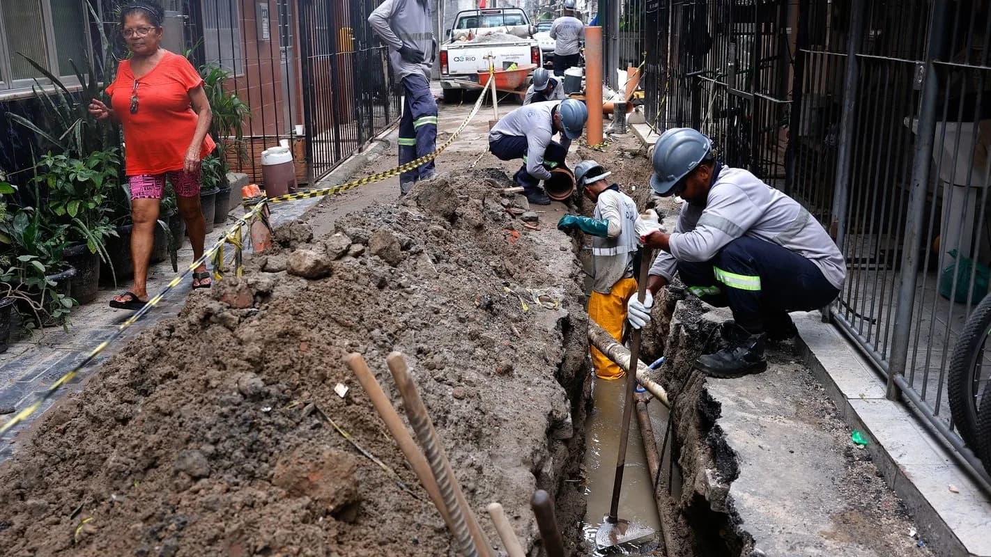 Trabalhadores de obra de saneamento em vala aberta na rua, com capacete e uniforme (foto ilustrativa)