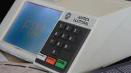 Urna eletrônica da Justiça Eleitoral exibindo a palavra FIM na tela, ao lado de material de votação