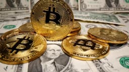 Moedas físicas representando criptomoeda sobre notas de dólar, foto ilustrativa do esquema de token associado à campanha de Flávio Bolsonaro
