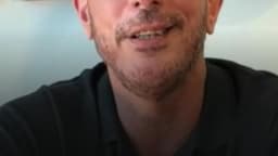 Abel Lumer, de óculos e camisa polo escura, fala olhando para a câmera, com parede decorada por peças de cerâmica ao fundo