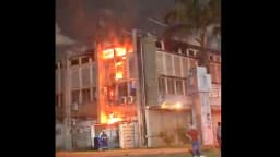 Chamas atingem prédio da UFPE durante incêndio à noite, com pessoa correndo próxima ao local