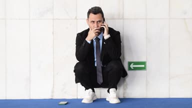 Foto de arquivo do senador Cleitinho, de terno preto e gravata, agachado ao lado de uma parede de mármore enquanto fala ao celular no Senado Federal
