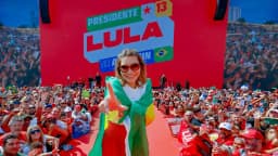 Janja com bandeira do Brasil em palco de campanha com painel Presidente Lula, foto de arquivo do lançamento da campanha em agosto