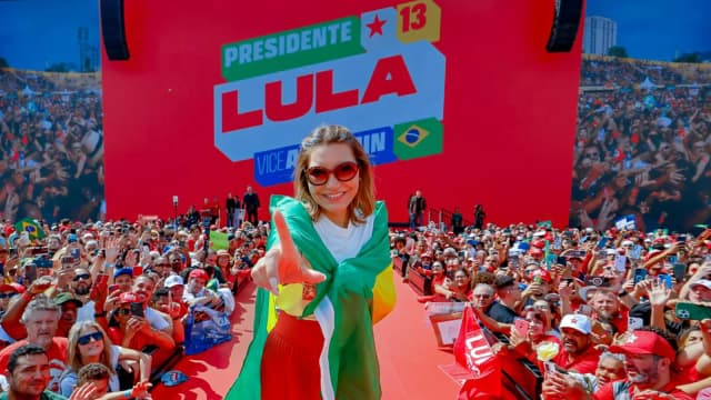 Janja com bandeira do Brasil em palco de campanha com painel Presidente Lula, foto de arquivo do lançamento da campanha em agosto