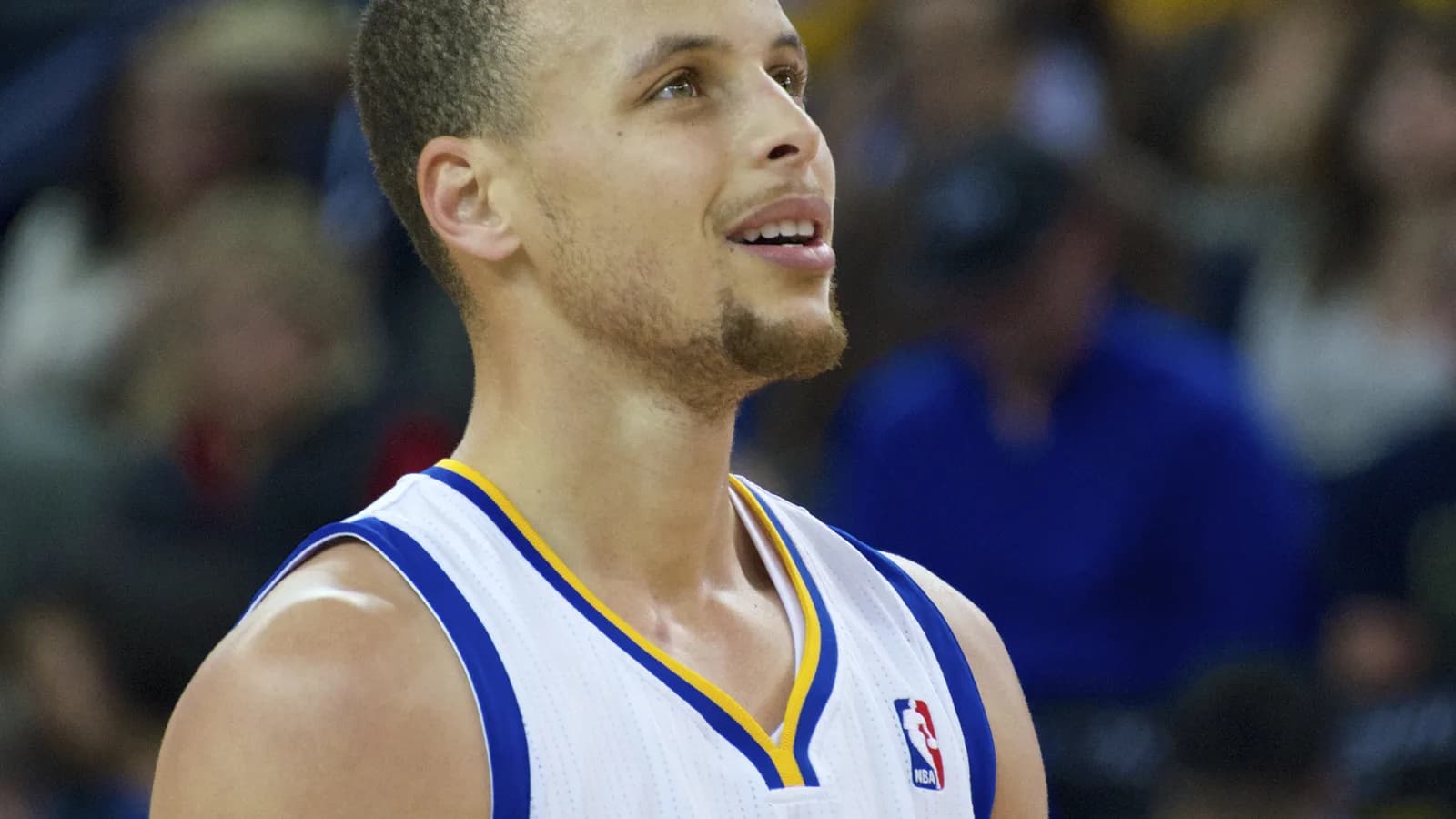 Stephen Curry em close, olhando para cima, com o uniforme do Golden State Warriors