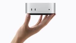 Mão segurando o novo Mac mini da Apple, mostrando a parte frontal com indicadores luminosos