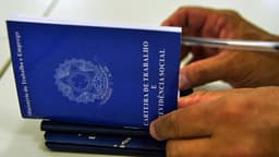 Mãos de uma pessoa segurando uma Carteira de Trabalho e Previdência Social sobre outras carteiras empilhadas, em imagem de arquivo