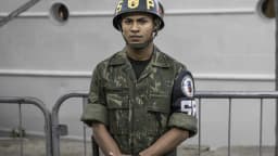 Policial militar fardado em frente a grade de contenção