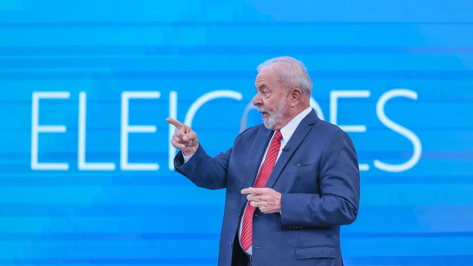 Lula gesticula durante debate de TV eleitoral, de pé em palco com fundo azul escrito Eleições (foto de arquivo)