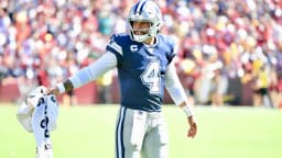Dak Prescott, quarterback do Dallas Cowboys, em campo com uniforme azul do time, gesticulando durante partida da NFL