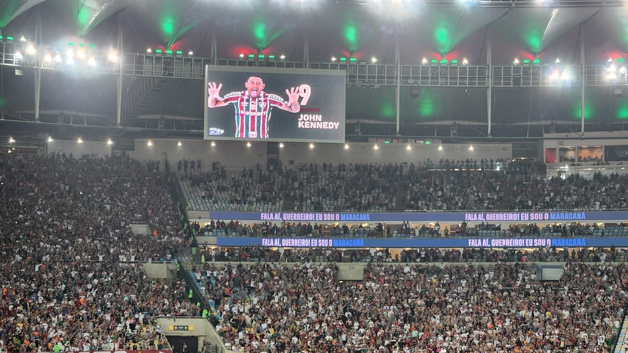 Torcida do Fluminense no Maracanã lotado com imagem de John Kennedy exibida no telão do estádio