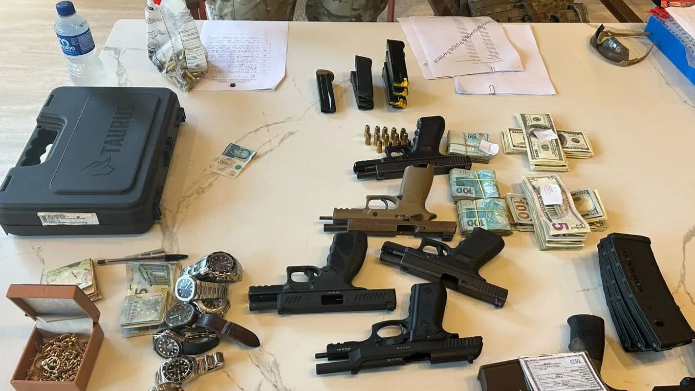 Armas, dinheiro e relógios apreendidos pela Polícia Federal sobre uma mesa