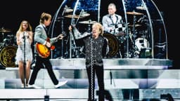 Rod Stewart canta em cima do palco durante show, com banda ao fundo