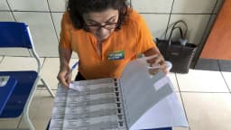 Mesária de uniforme laranja confere lista de eleitores em mesa de votação, em foto de arquivo de 2018