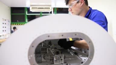 Estudante de curso técnico, de óculos de proteção e luvas, trabalha em equipamento dentro de um laboratório; imagem de arquivo