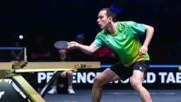 Hugo Calderano em ação durante partida de tênis de mesa, uniforme verde do Brasil