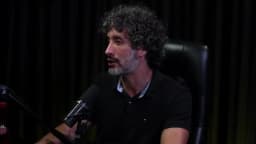 Carlos Eduardo Grimaldi fala recostado na cadeira, em perfil levemente lateral, em estúdio de podcast com cortina escura ao fundo