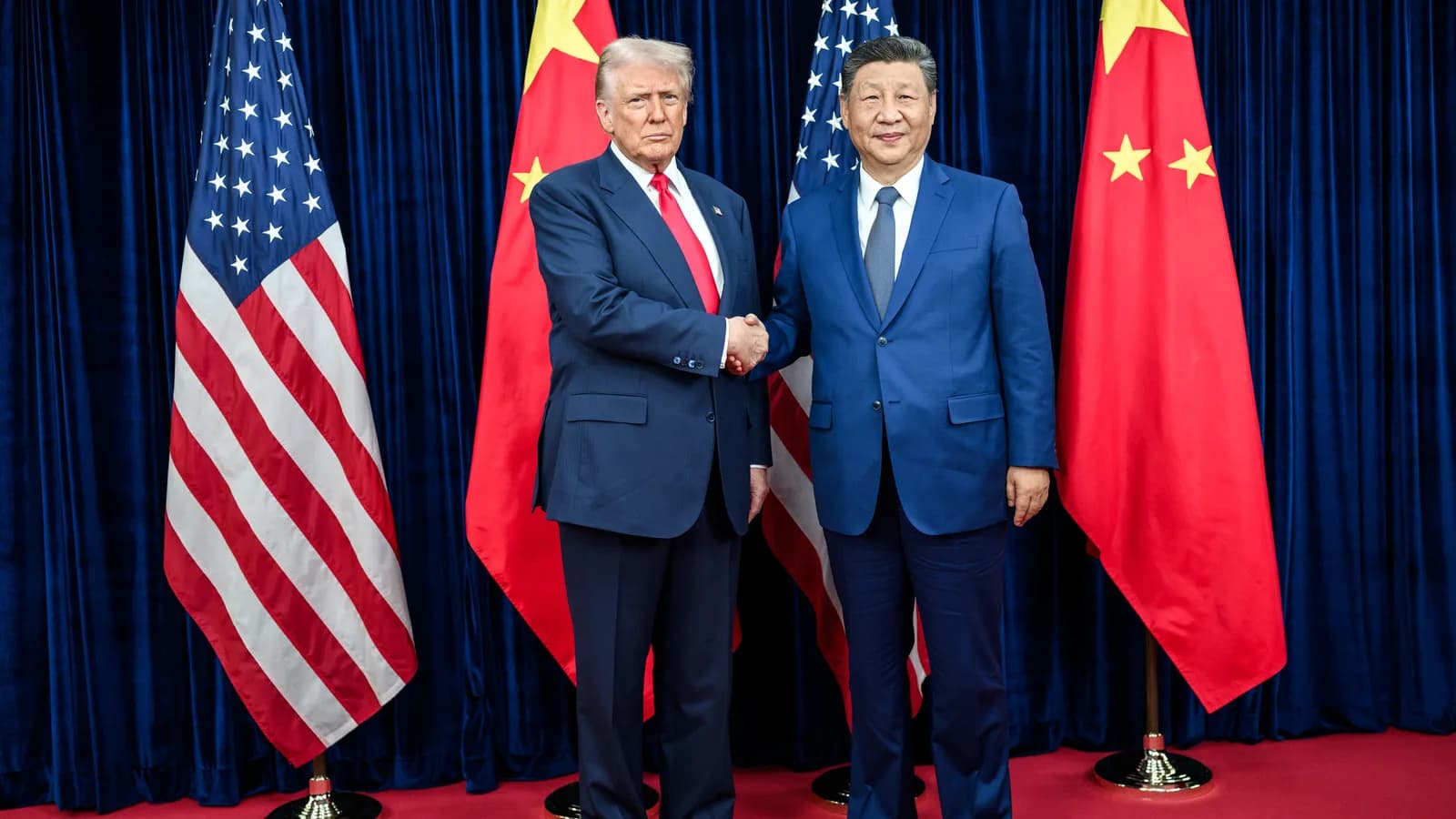 Donald Trump e Xi Jinping apertam as mãos diante das bandeiras dos Estados Unidos e da China
