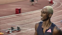 Alison dos Santos sorri em pista de atletismo durante competição, com blocos de largada ao fundo