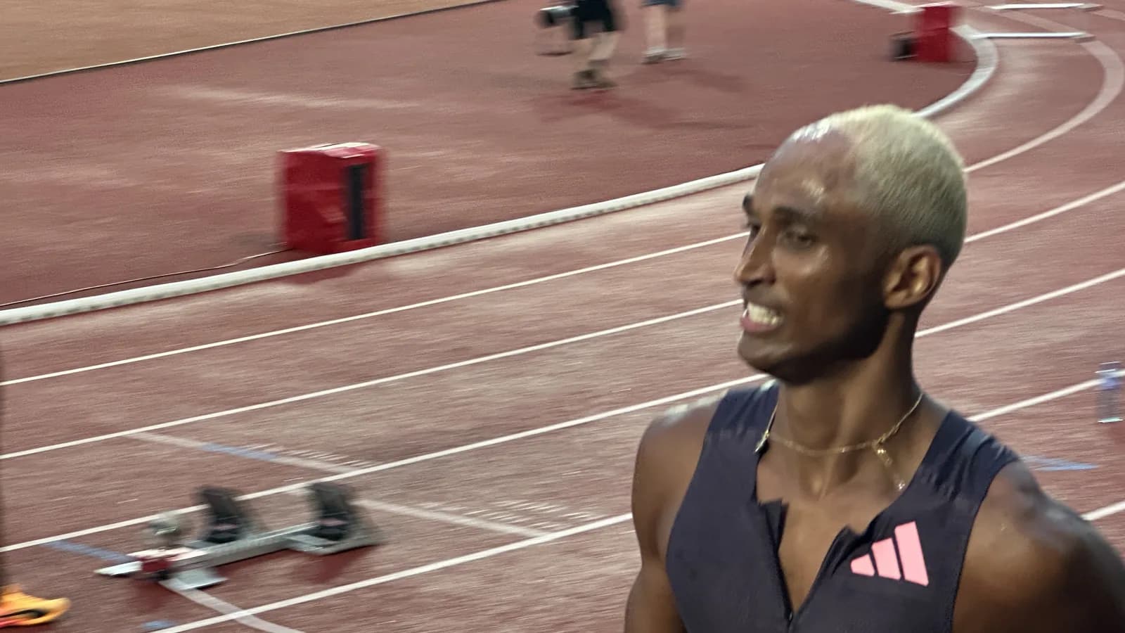 Alison dos Santos sorri em pista de atletismo durante competição, com blocos de largada ao fundo