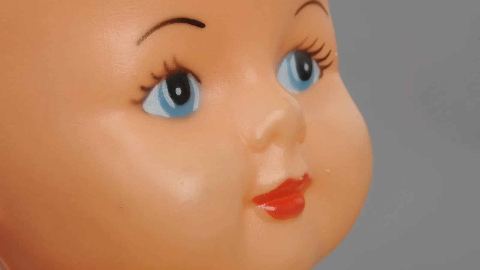 Close-up do rosto de um boneco antigo, com olhos pintados e expressão fixa