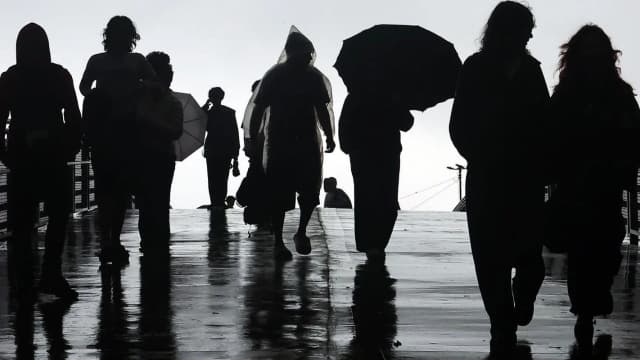 Pedestres caminham sob chuva em São Paulo, com guarda-chuvas, à noite